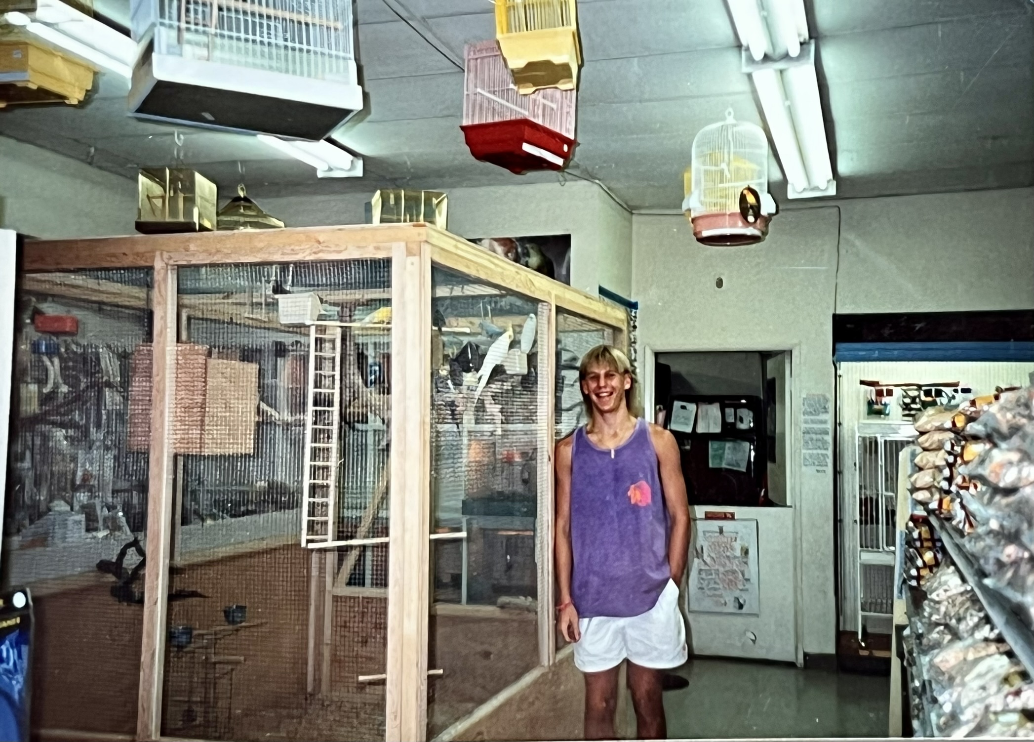 A young Brian Robinson standing in front of a custom aviary he built inside the family pet store, bird cages hanging from the ceiling.